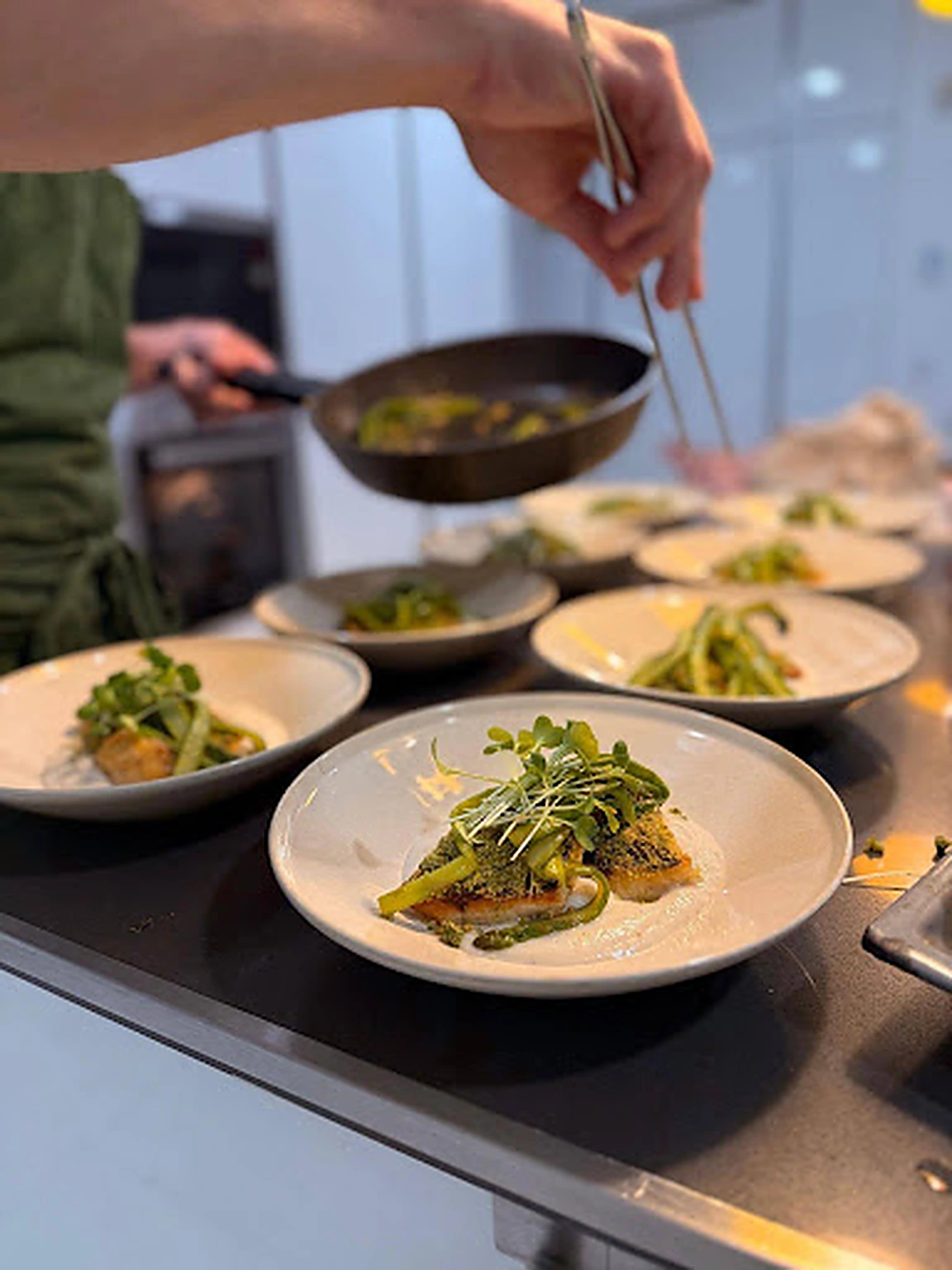 A Basil chef finishing a row of plated fish courses at the pass
