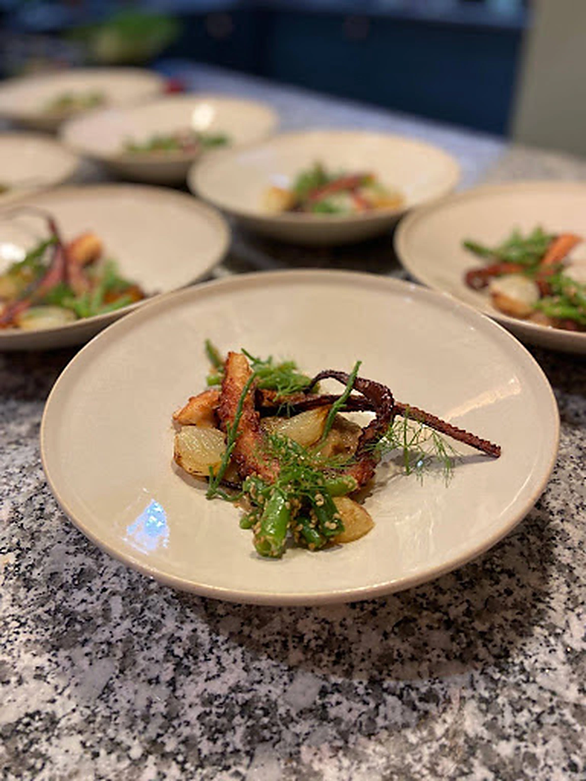 A plated octopus course with seasonal vegetables during catering service