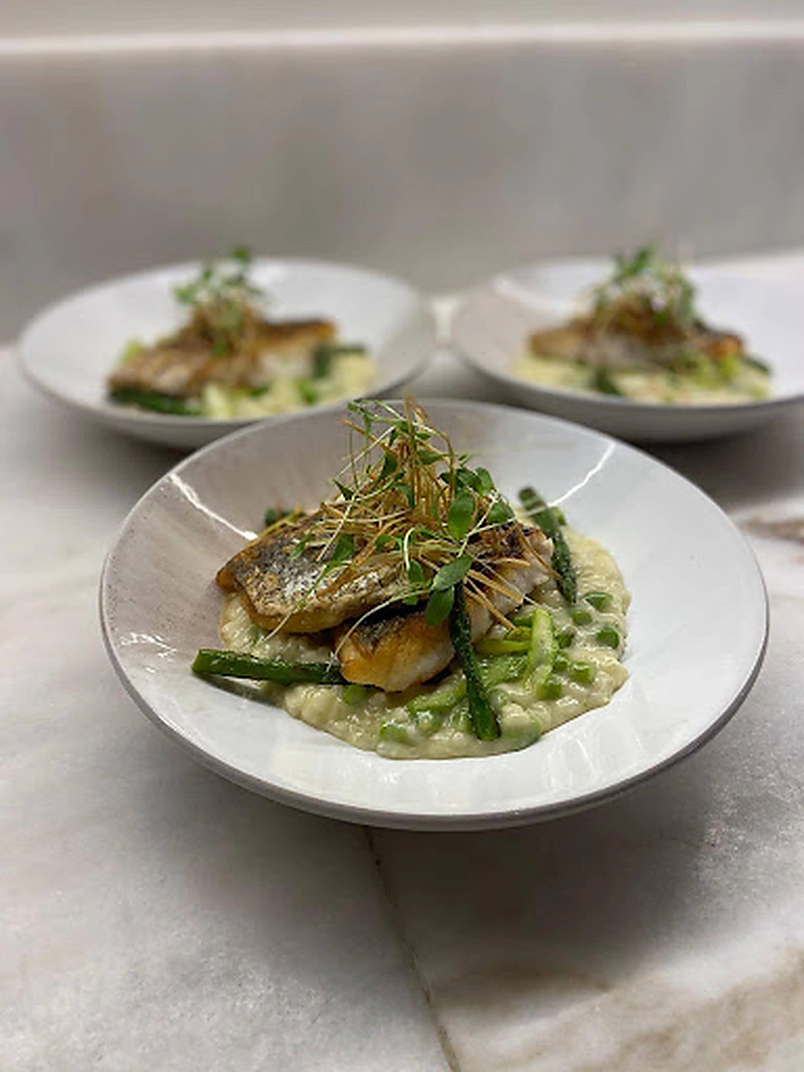 Three plates of fish with asparagus and herb risotto ready for catering service