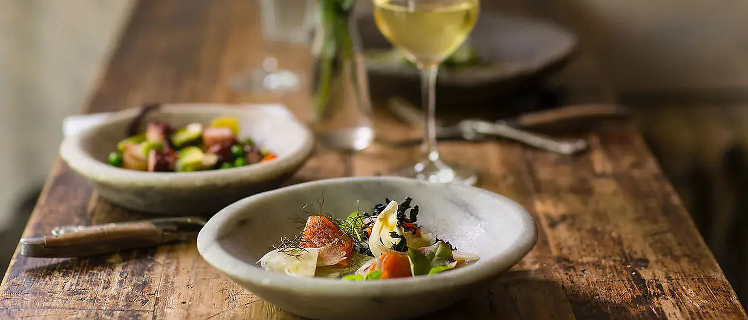 Two plated courses and a glass of white wine on a weathered wooden dining table