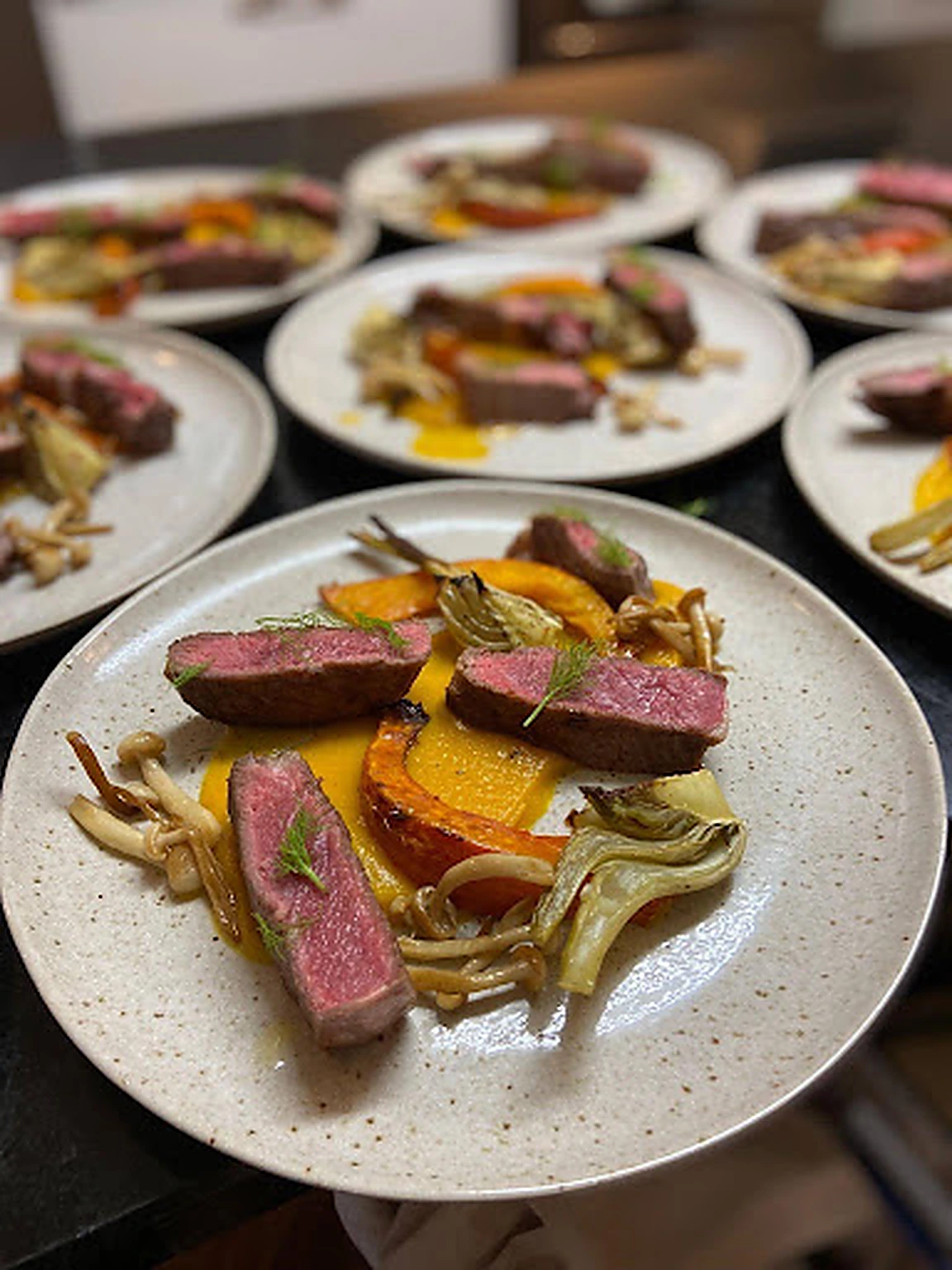 Plates of pink beef with squash, mushrooms and artichoke ready for service