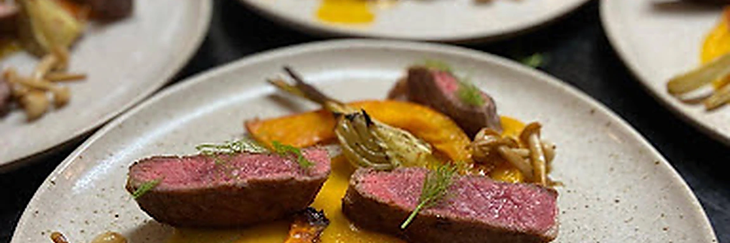 Plates of pink beef with squash, mushrooms and artichoke ready for service
