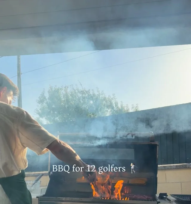 A chef tending an open flame in an outdoor grill under Algarve smoke and sky