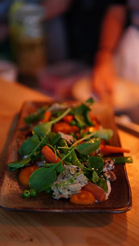 A long ceramic plate of vegetables and shellfish photographed on a dinner table
