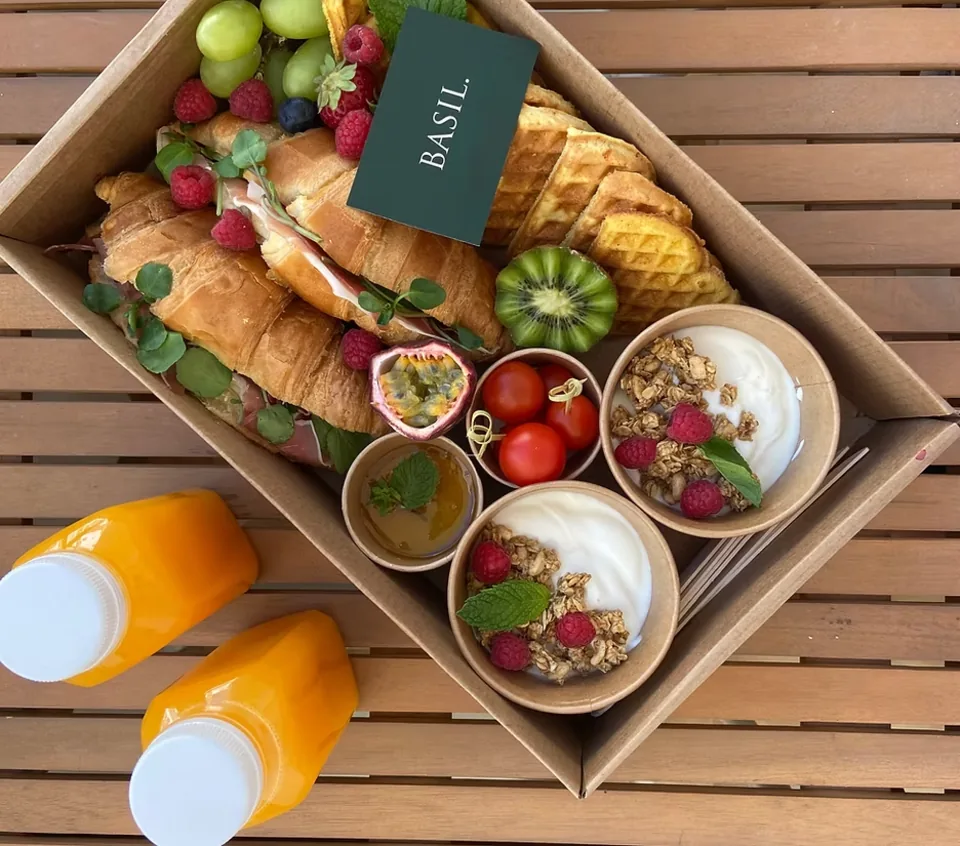 A Basil brunch box of croissants, waffles, fruit, granola and fresh orange juice on a terrace table