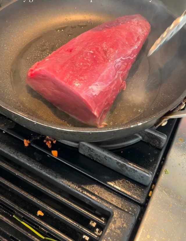 A thick cut of beef resting in a hot steel pan