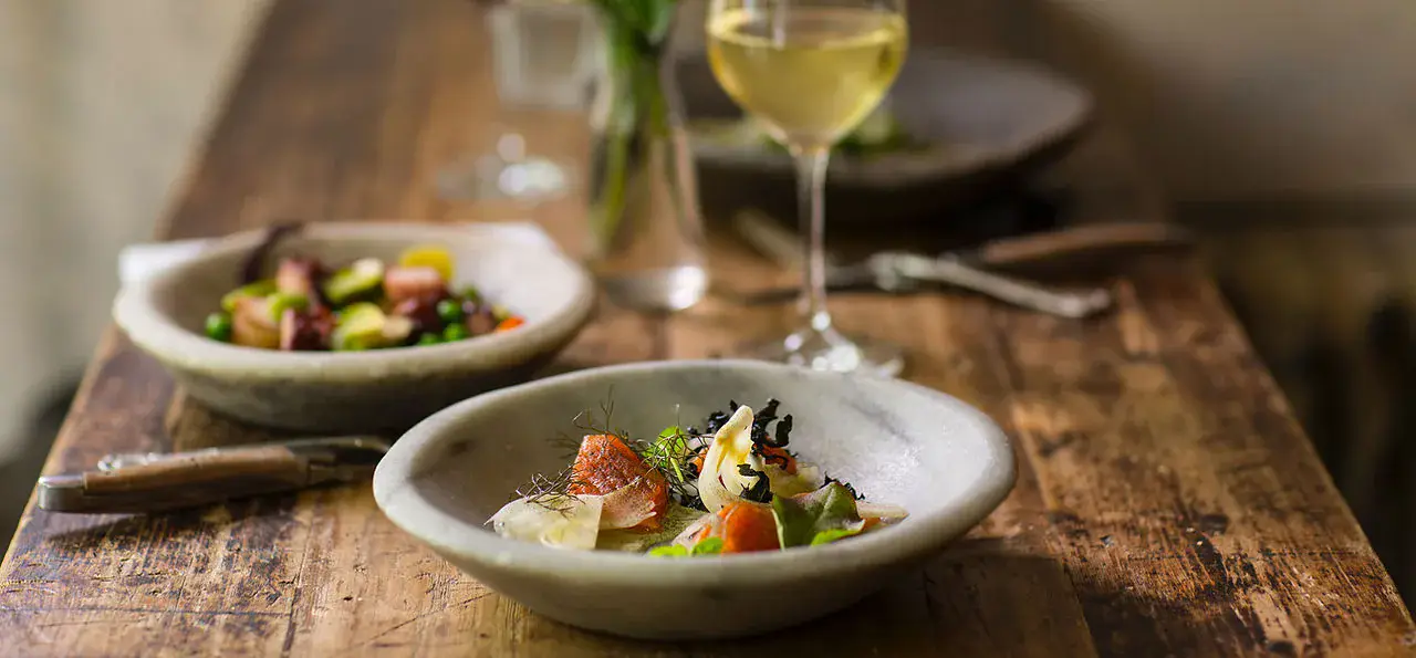Two plated courses and a glass of white wine on a weathered wooden dining table