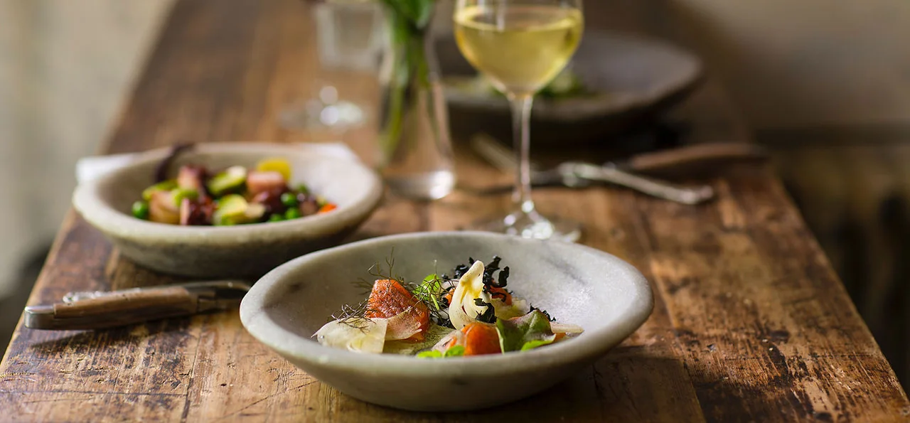 Two plated courses and a glass of white wine on a weathered wooden dining table